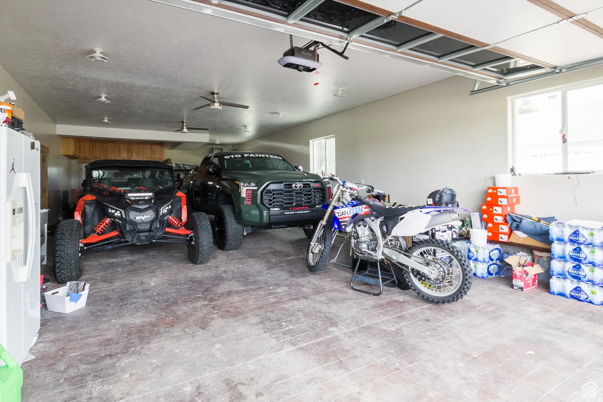 Spacious attached garage featuring multiple ceiling fans, recessed lighting, and ample natural light from two windows