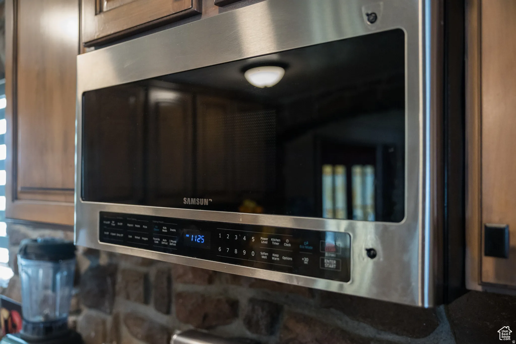 Stainless steel over-the-range microwave with integrated controls, surrounded by wood cabinetry and a stone-finish backsplash