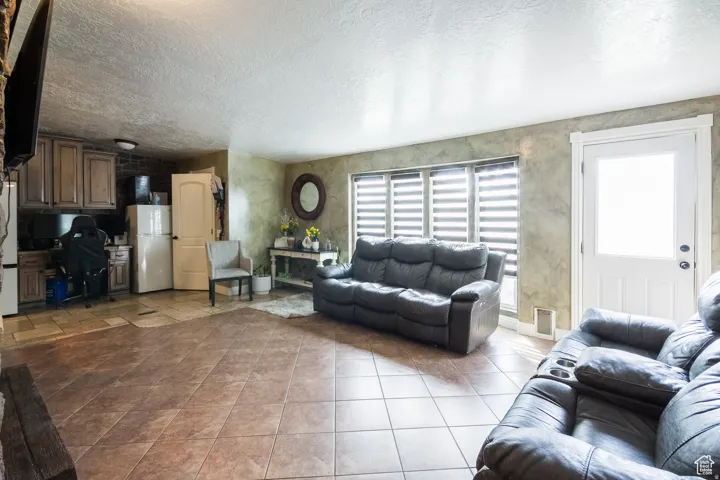 Spacious interior featuring large format tile flooring, a white paneled door with frosted glass, and multiple windows with horizontal blinds