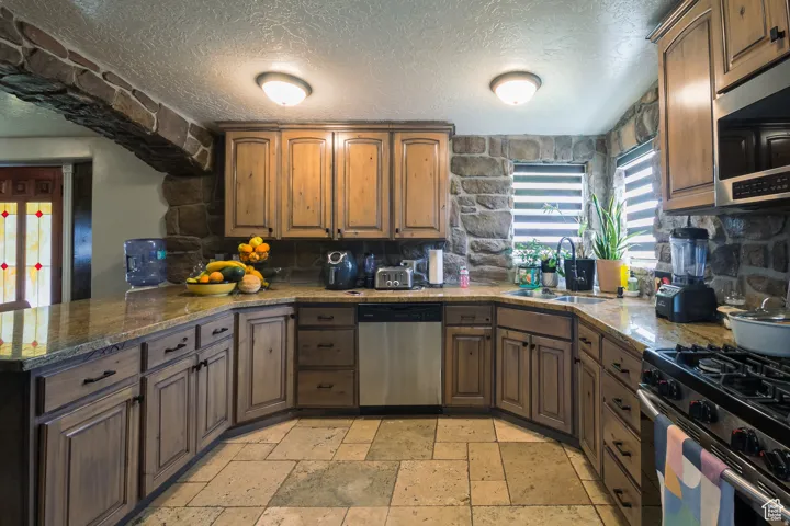 Kitchen featuring stone wall accents, wood-finish cabinetry, stone tile flooring, and integrated stainless steel appliances