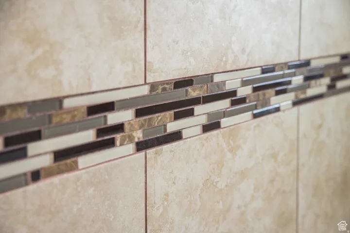Large format beige wall tile with a mosaic accent band featuring varied rectangular tiles in earth tones