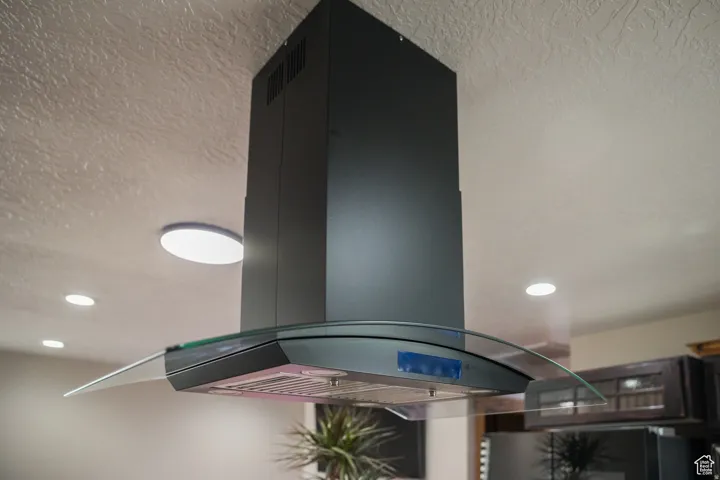 Modern island range hood with a curved glass canopy, metallic finish, and task lighting