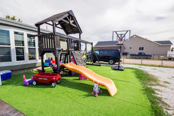 Spacious outdoor area featuring a wooden playset with a slide, a basketball hoop, and artificial turf surfacing