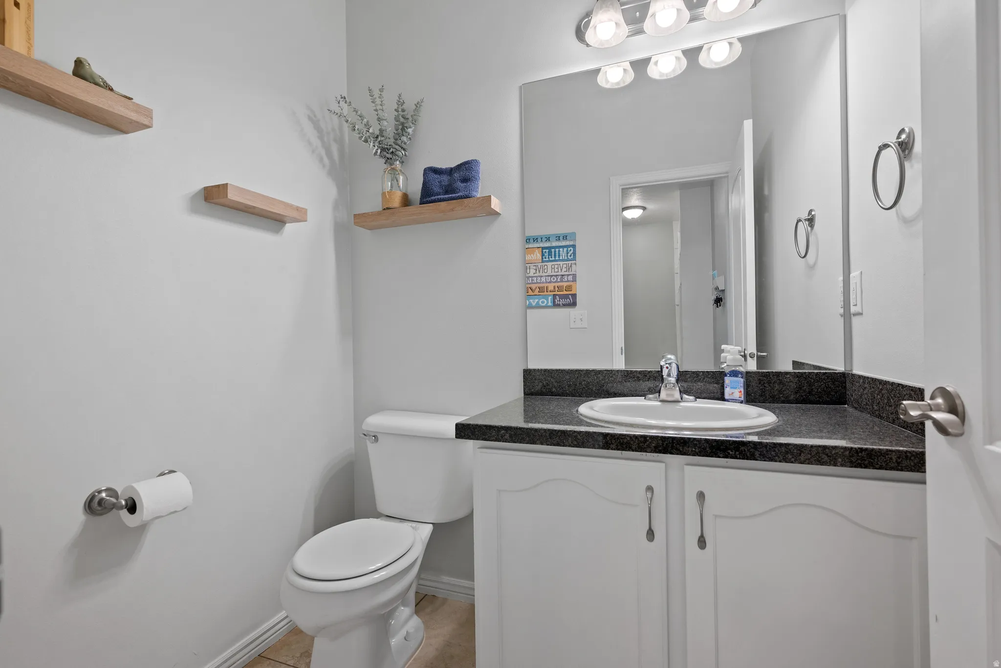 Vanity with dark countertop and undermount sink, framed by a large wall mirror and overhead light fixture