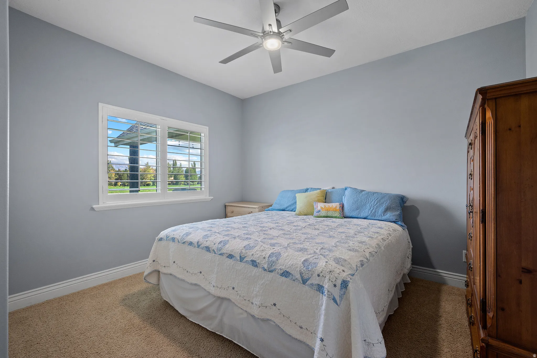 Carpeted room with a ceiling fan, a window featuring plantation shutters, and light blue wall tones