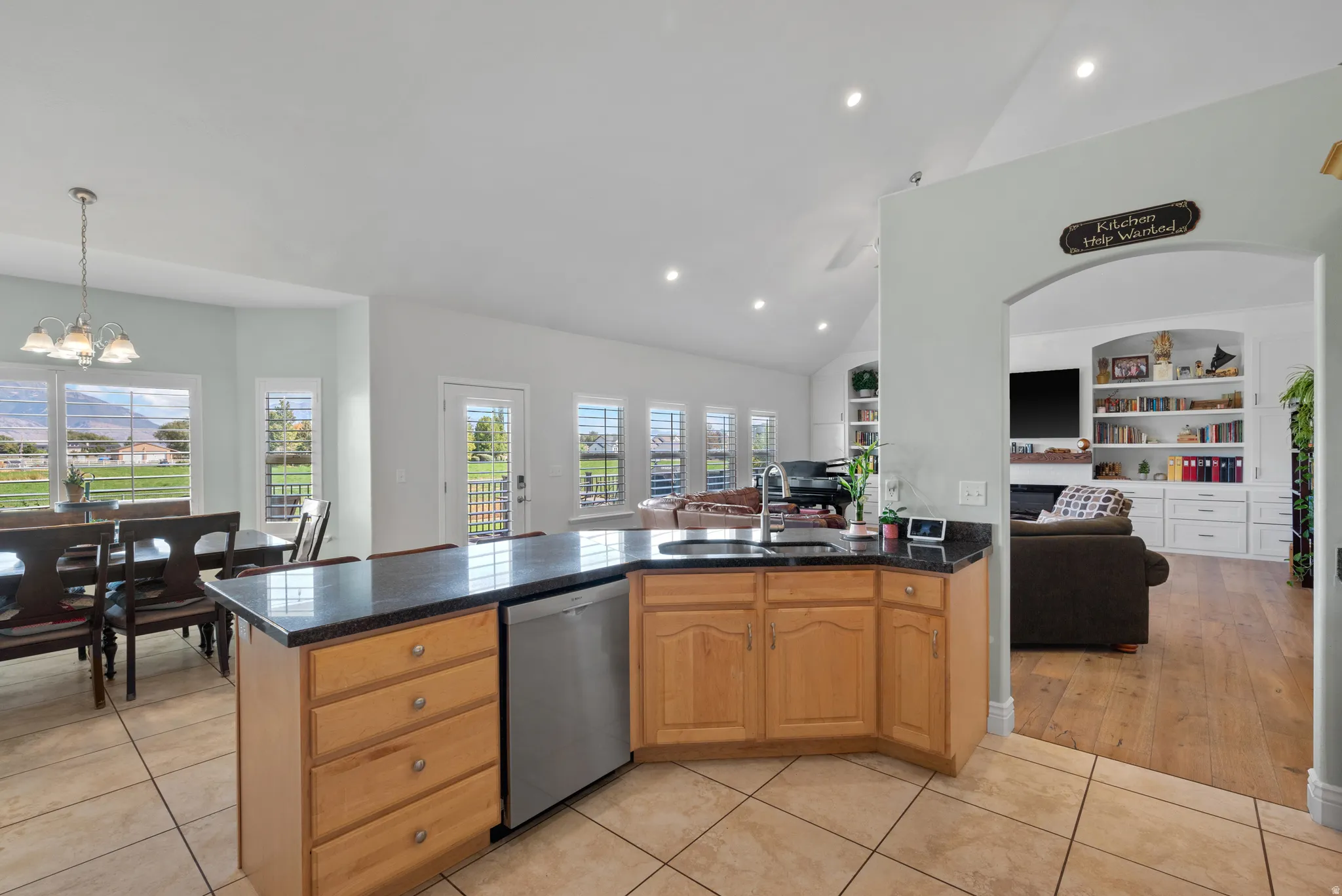 Kitchen island with a dark countertop and light wood-finish cabinetry, featuring an integrated stainless steel dishwasher