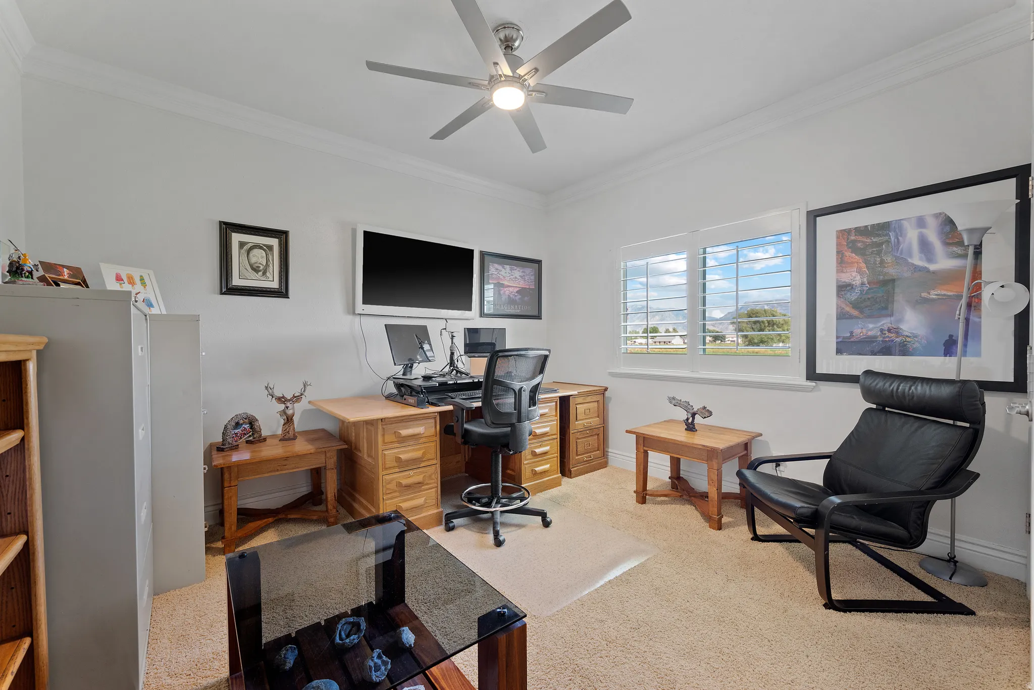 Light-filled room featuring a ceiling fan, crown molding, plantation shutters, and carpeted flooring
