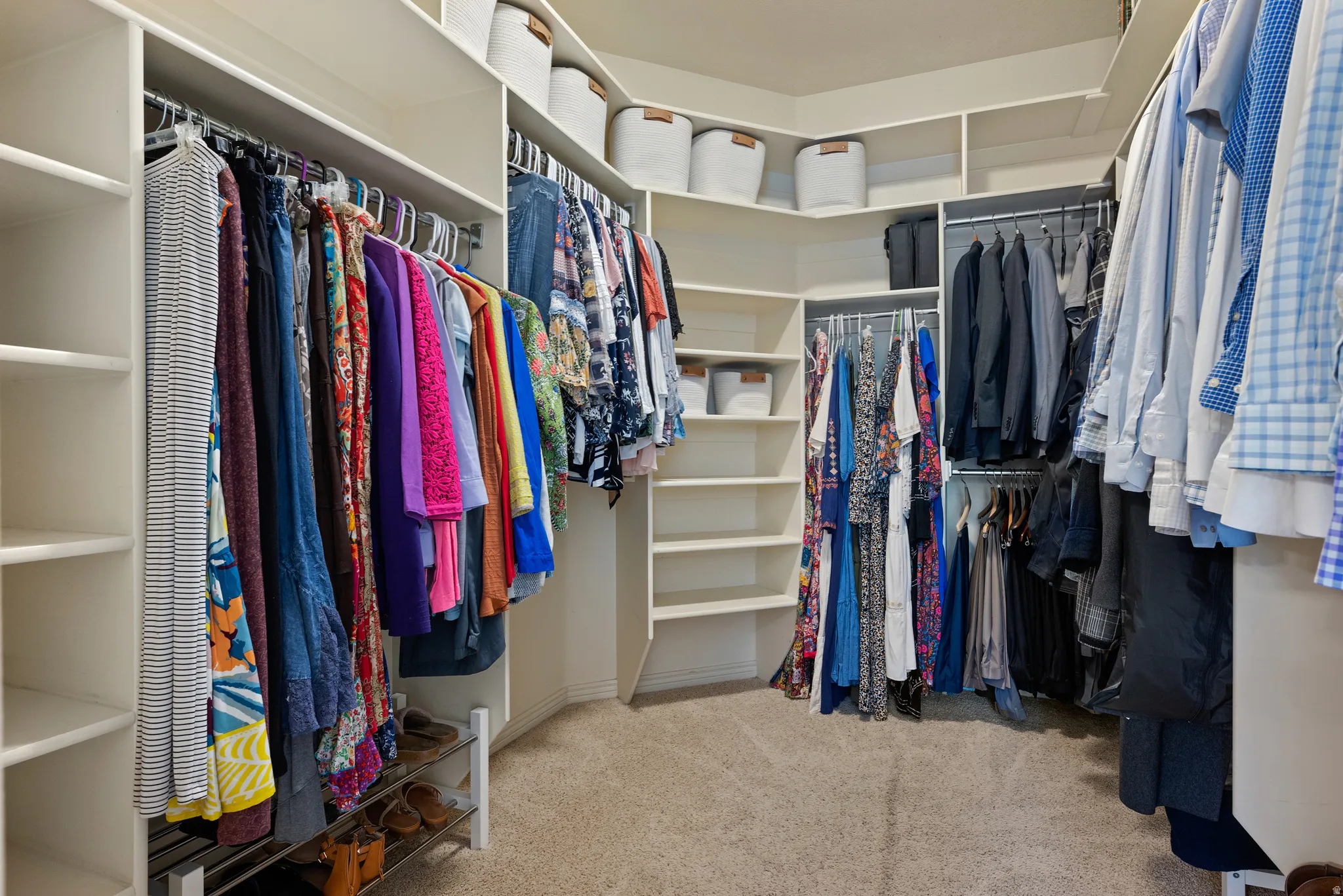 Walk-in closet featuring built-in shelving, multiple hanging rods, corner storage, and light-toned carpet flooring