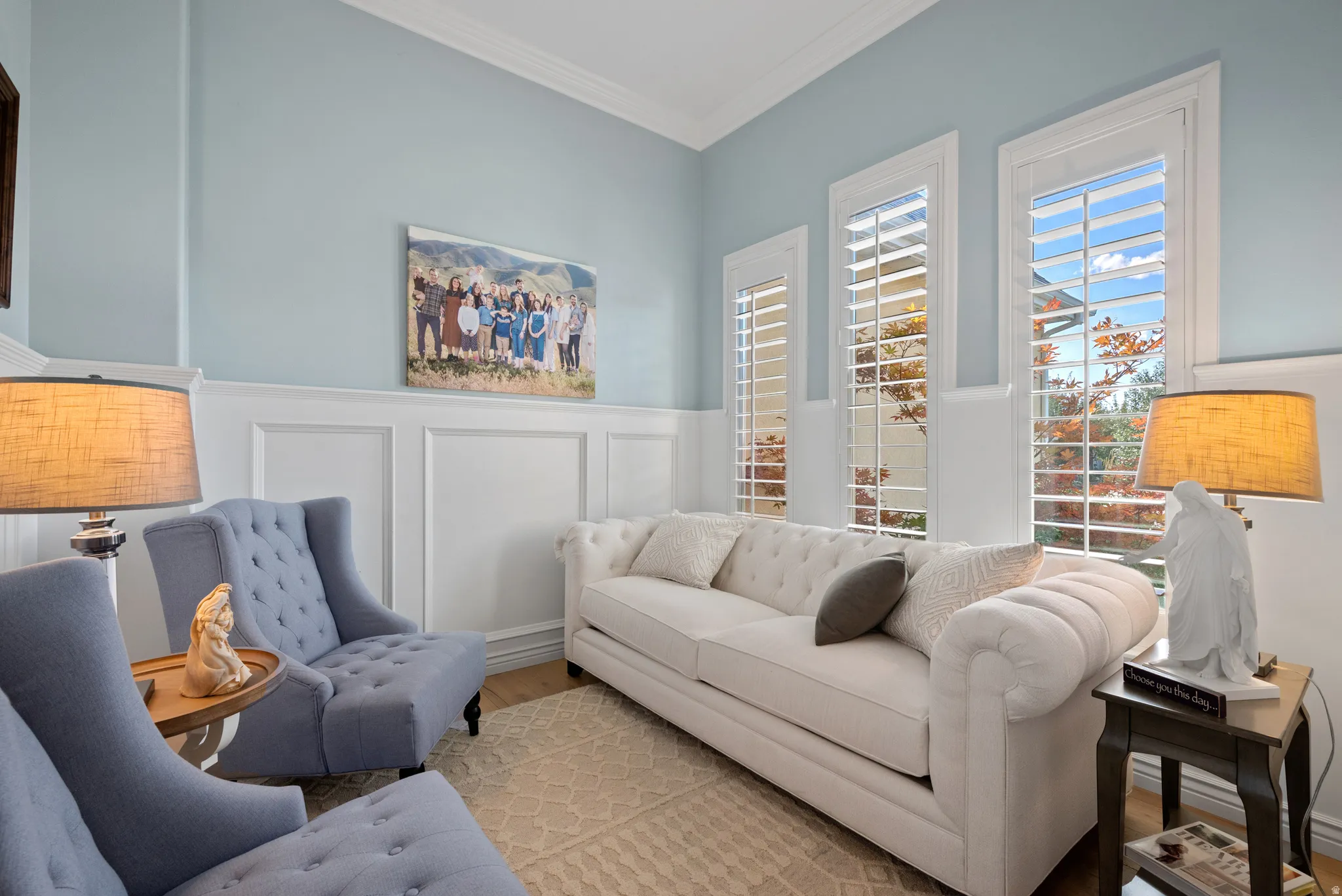 Living area featuring light blue wall paint, white wainscoting, and crown molding