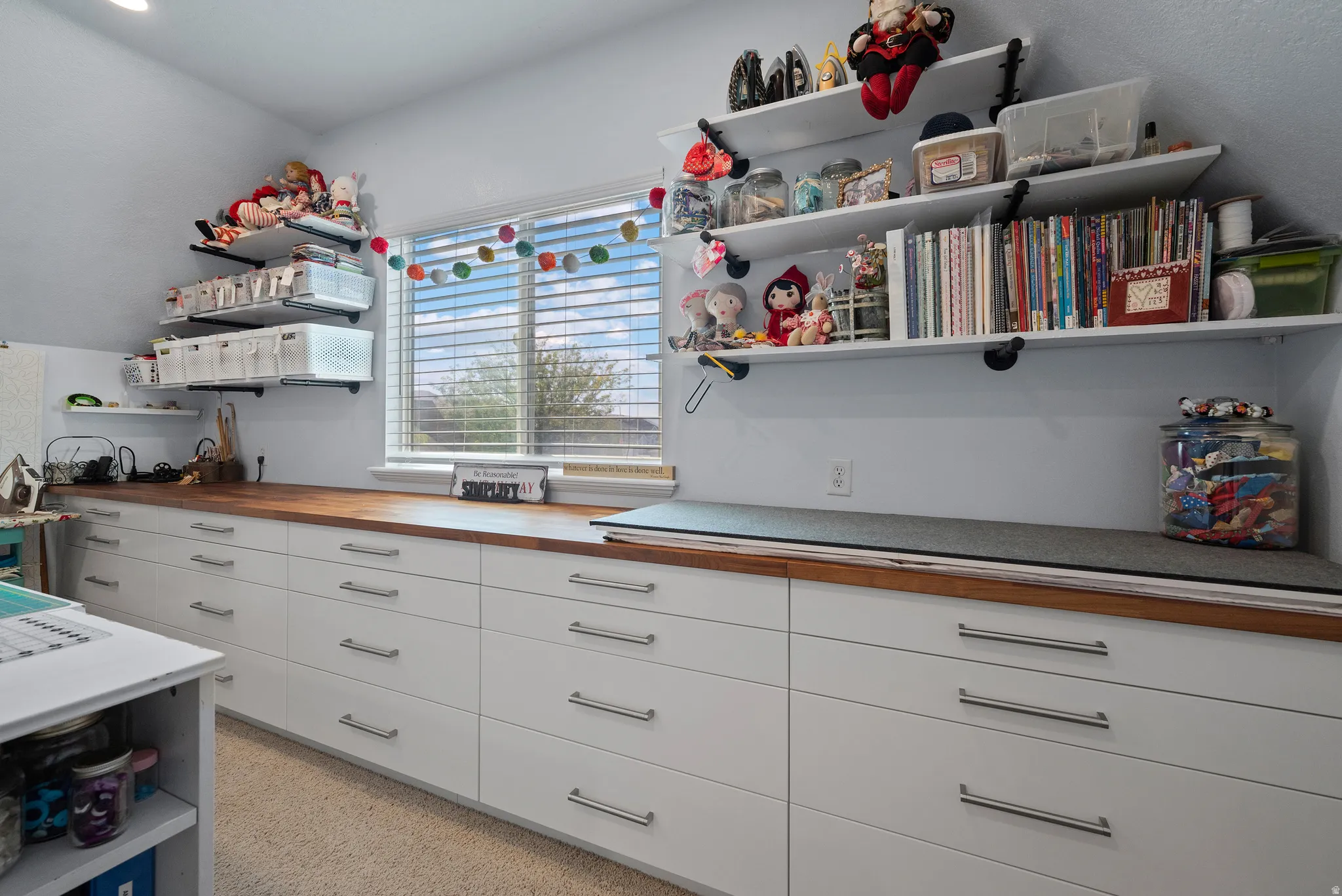 Dedicated room featuring extensive built-in cabinetry with wood-finish countertops, wall-mounted shelving, and a bright window with blinds
