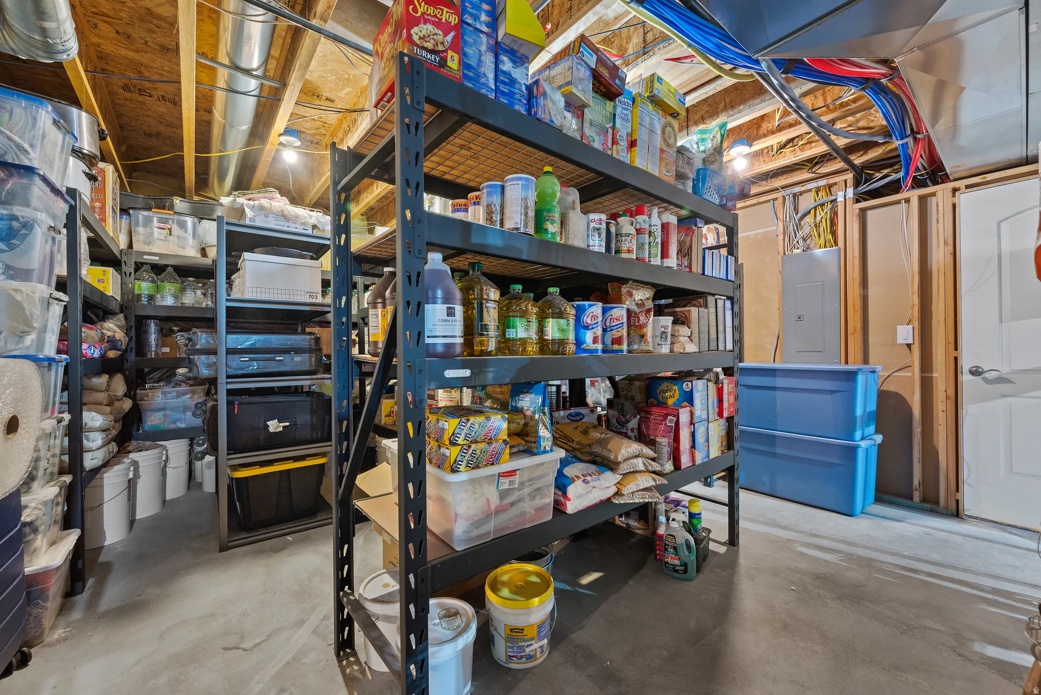 Unfinished basement area featuring exposed ceiling joists and ductwork, concrete flooring, and a white interior door
