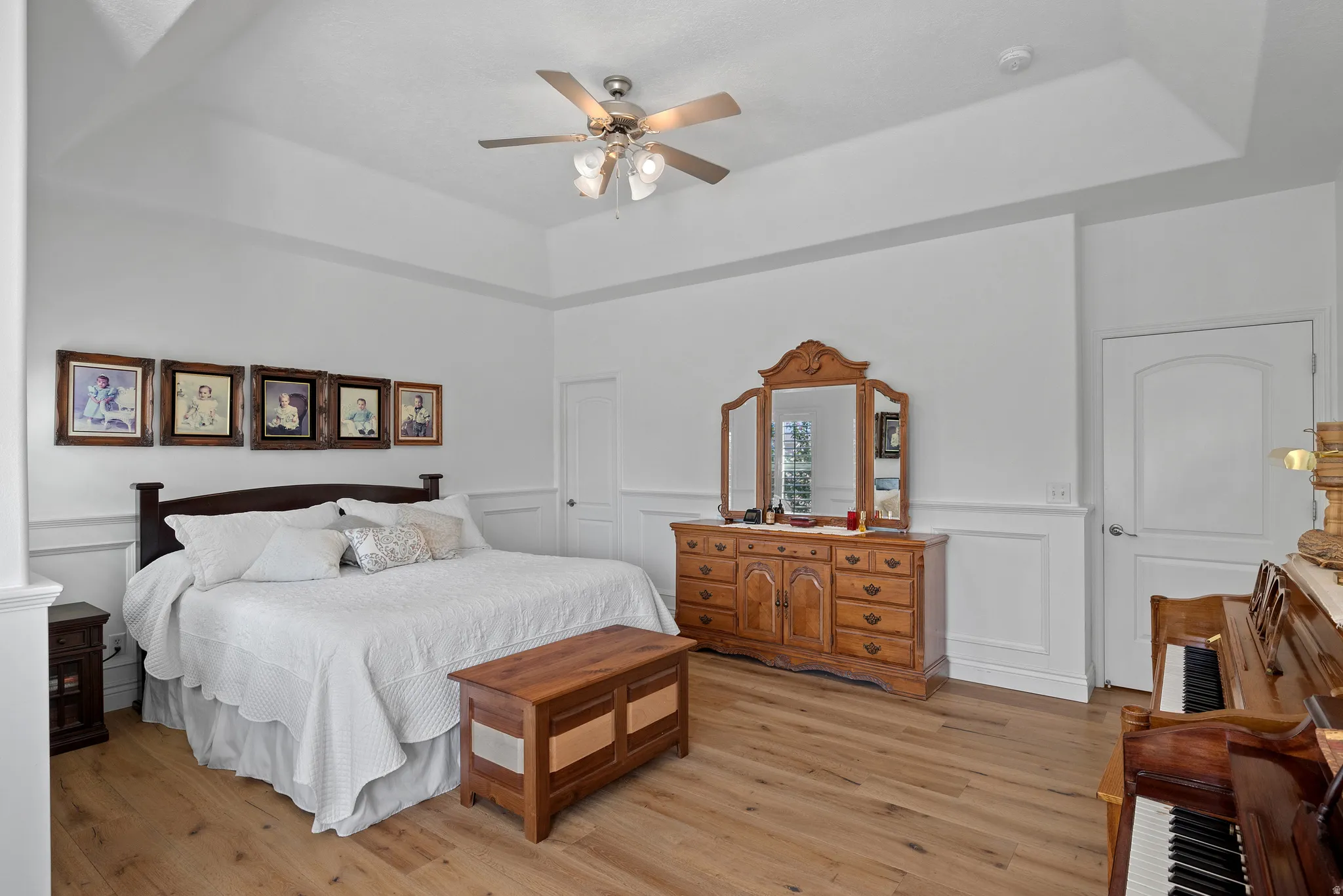 Spacious bedroom featuring a tray ceiling, wood-finish flooring, wainscoting, and a ceiling fan with integrated lighting
