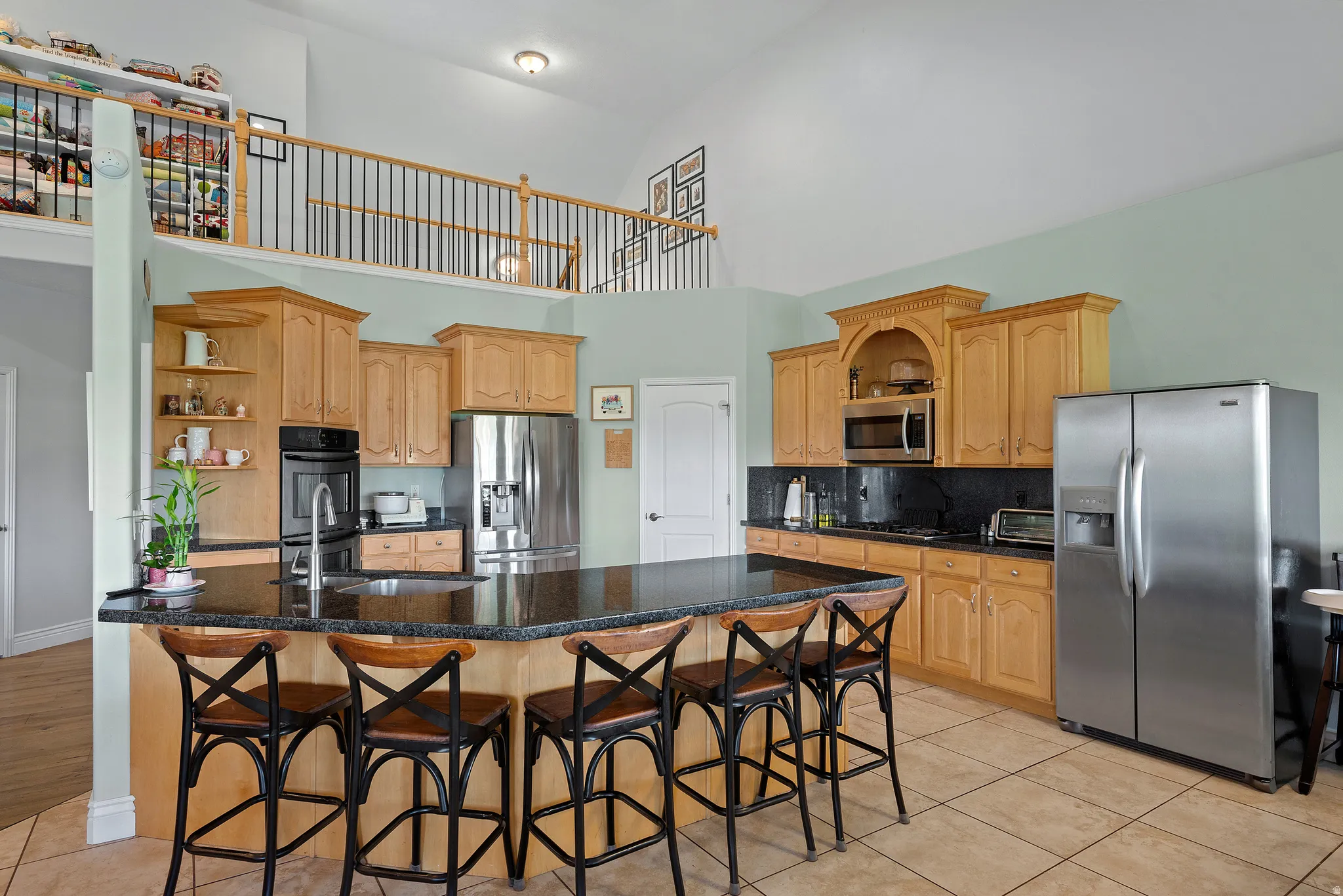 Kitchen featuring a large central island with seating, natural wood-finish cabinetry, stainless steel appliances, and a dark stone-finish countertop