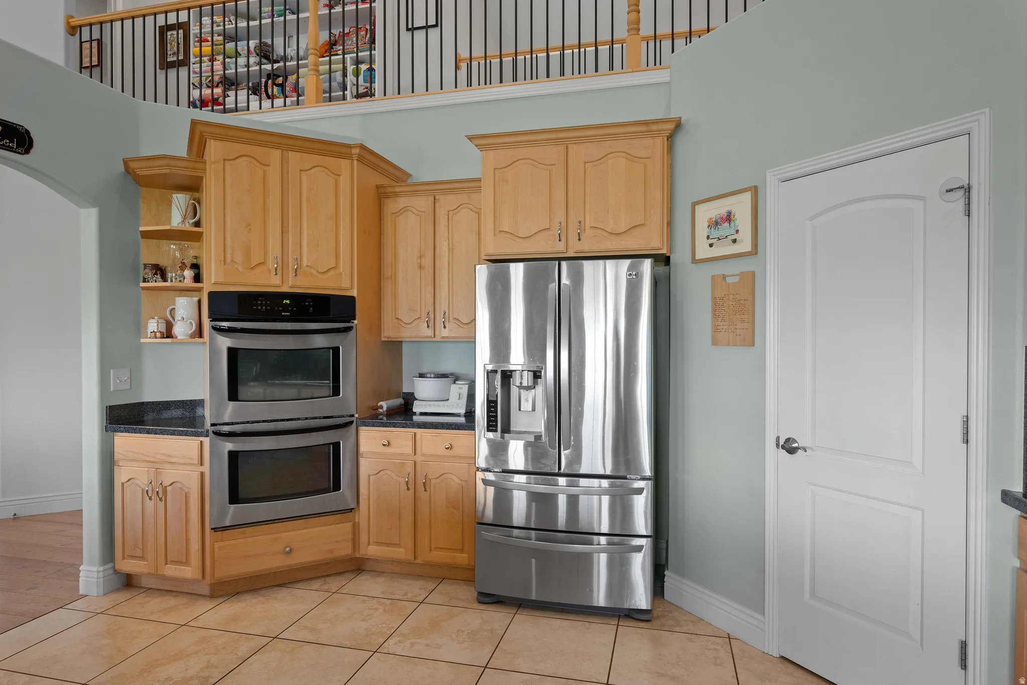 Kitchen area featuring light wood cabinetry, dark countertops, and stainless steel double ovens