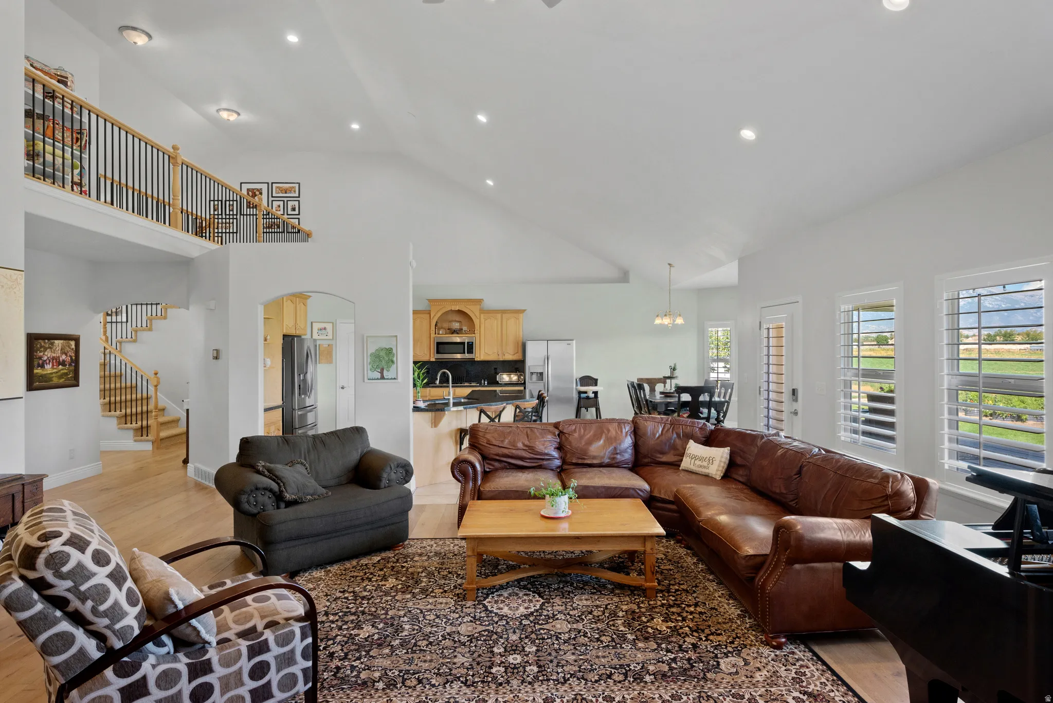 Vaulted great room featuring light wood-finish flooring, recessed lighting, and a prominent staircase with wood newel posts and black metal balusters