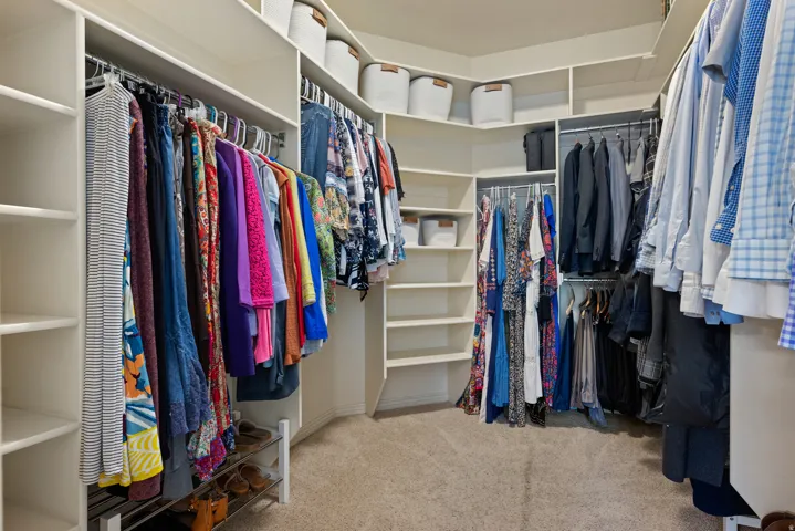 Walk-in closet featuring built-in shelving, multiple hanging rods, corner storage, and light-toned carpet flooring