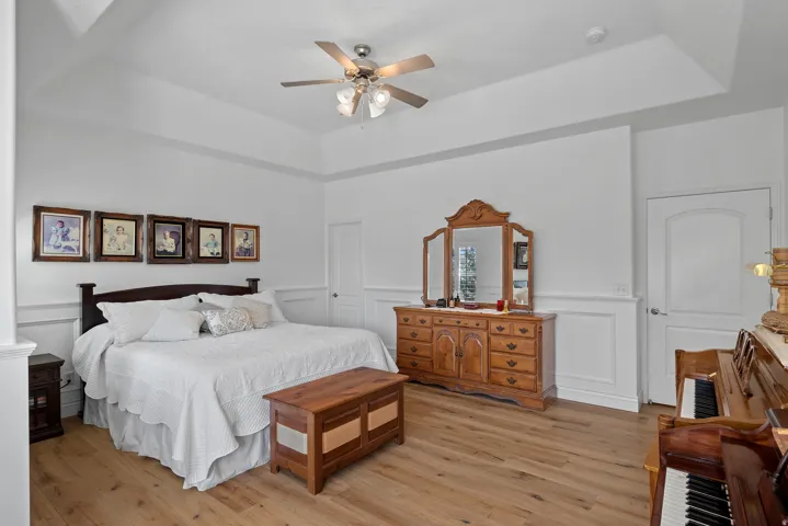 Spacious bedroom featuring a tray ceiling, wood-finish flooring, wainscoting, and a ceiling fan with integrated lighting
