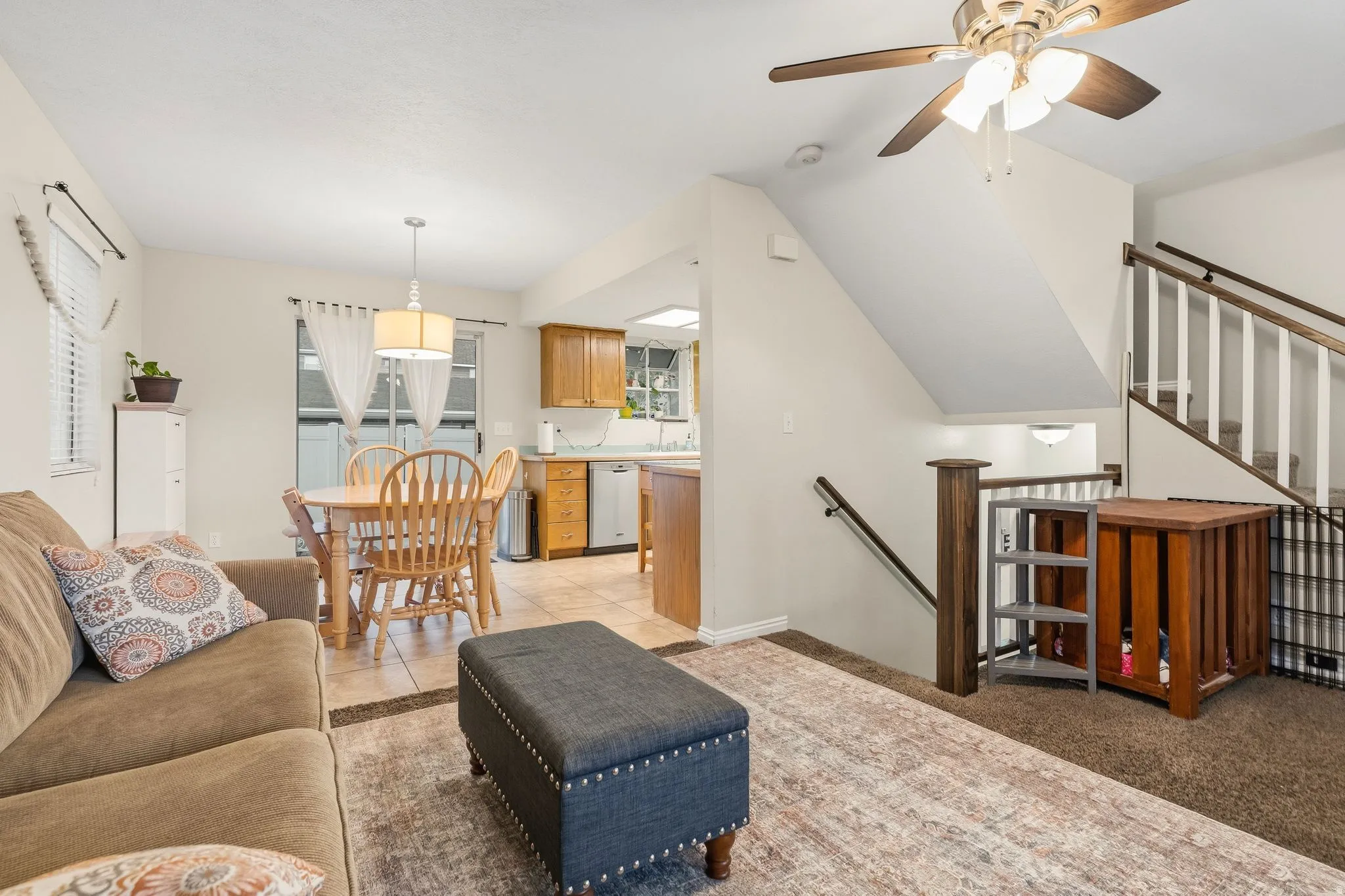Open-concept living area featuring a ceiling fan, light carpet and tile flooring, and a staircase with white balusters
