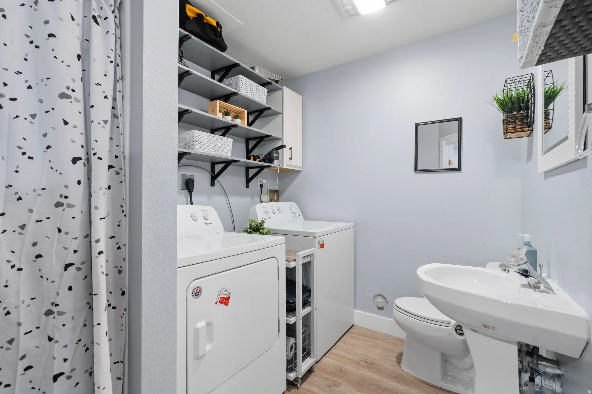 Compact utility space featuring wood-finish flooring, a white pedestal sink, a toilet, and integrated laundry appliances