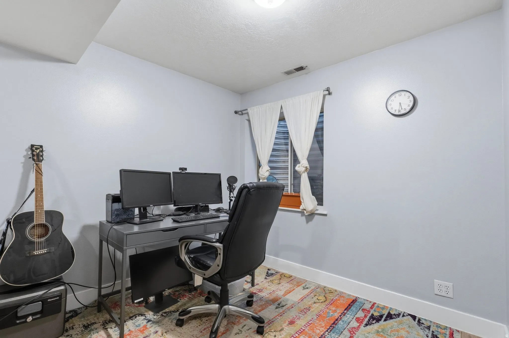 Office space featuring a window with white drapes, light blue walls, and white baseboards