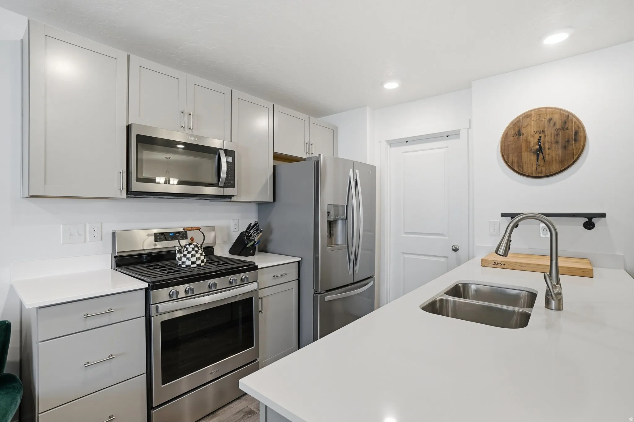 Modern kitchen featuring light gray cabinetry, stainless steel appliances, white countertops, and a dual-basin undermount sink with a pull-down faucet