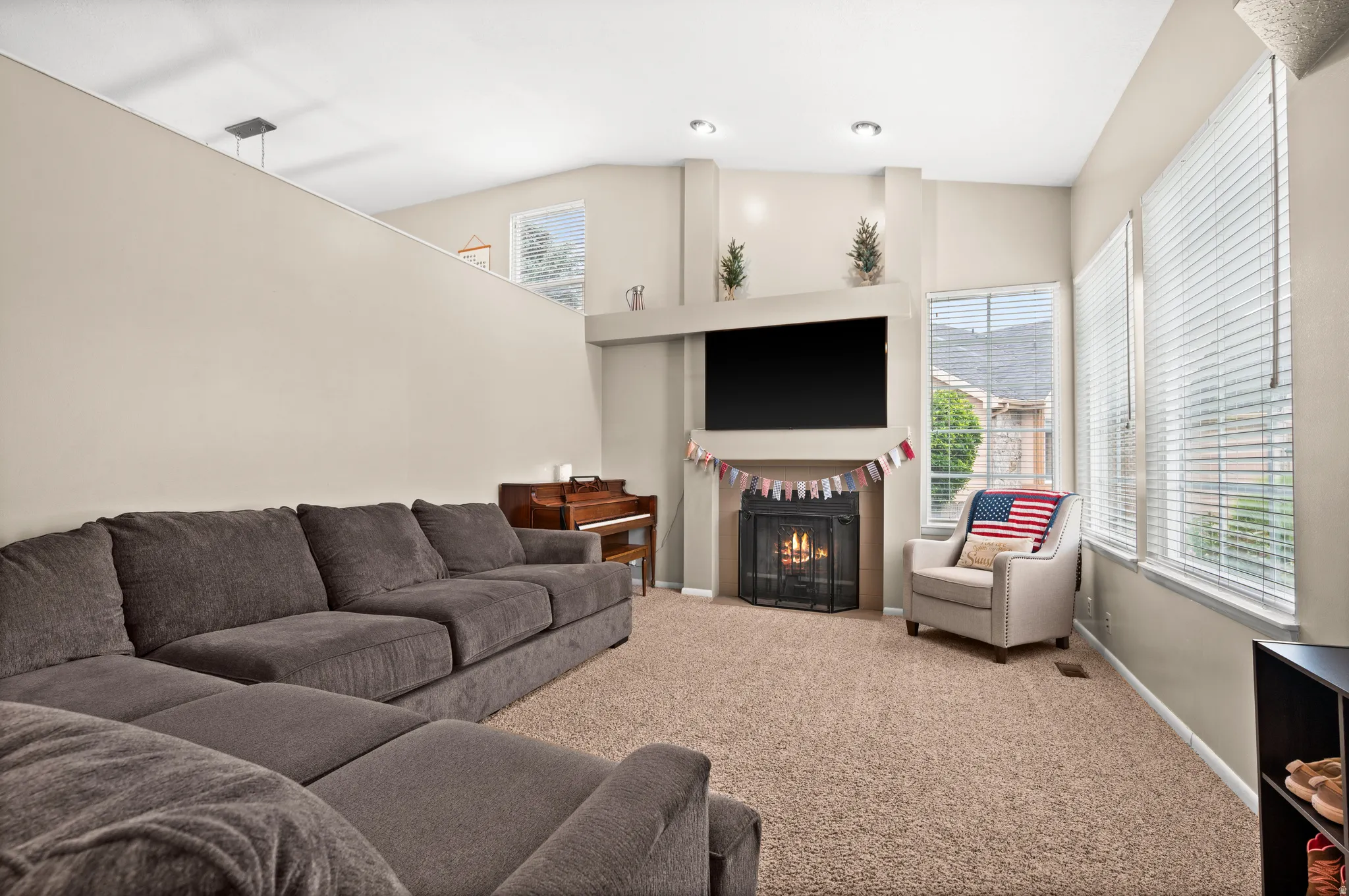 Living area featuring a fireplace with a decorative mantel, neutral-toned carpeting, and multiple windows with blinds