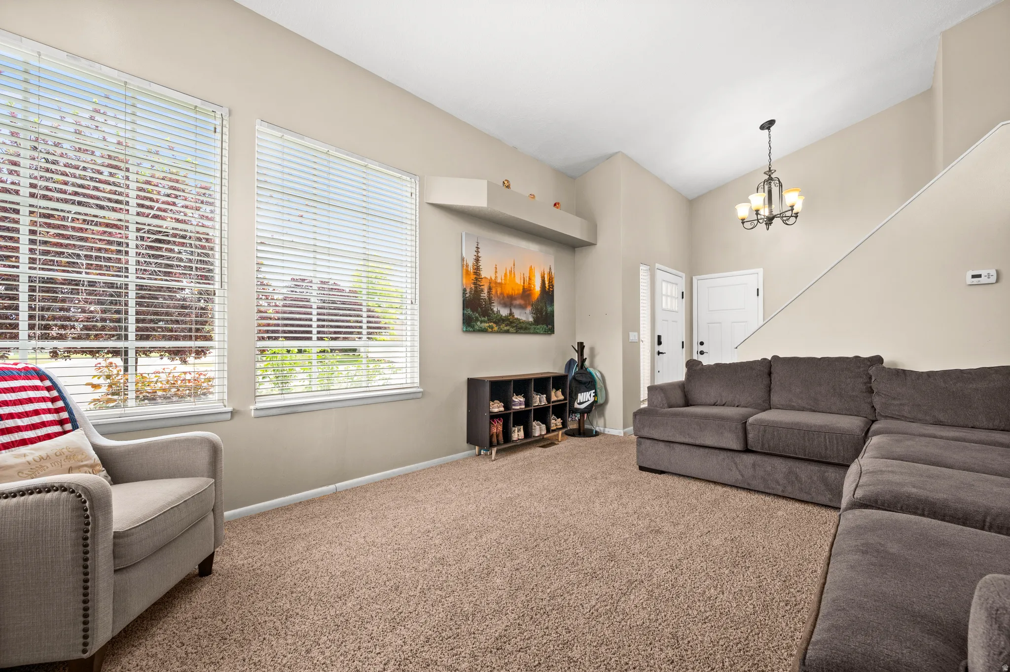 Living area featuring two large windows with blinds, vaulted ceilings, a chandelier, and carpet flooring