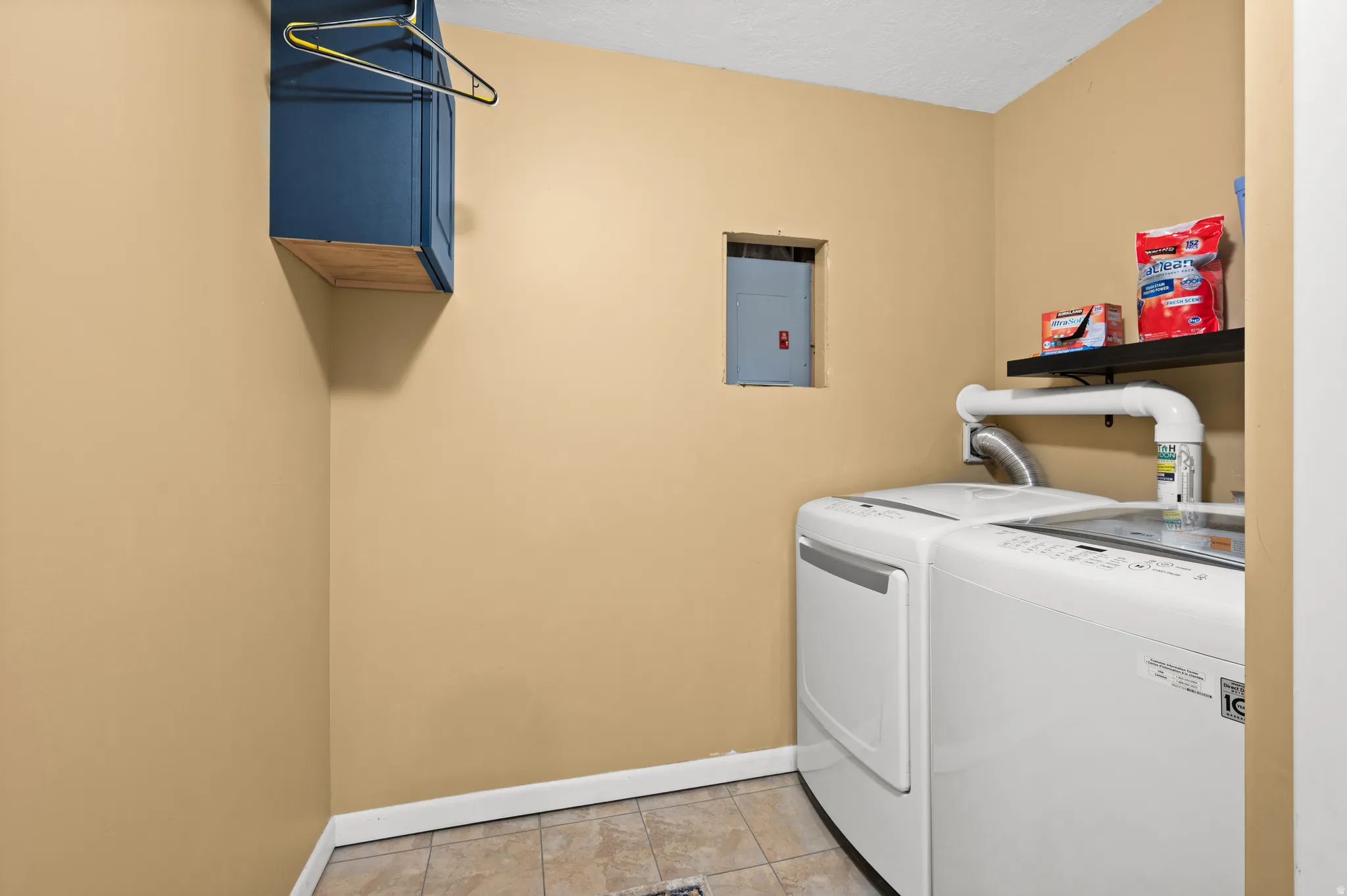 Dedicated laundry area featuring ceramic tile flooring, light tan wall color, a wall-mounted shelf, and an overhead storage cabinet