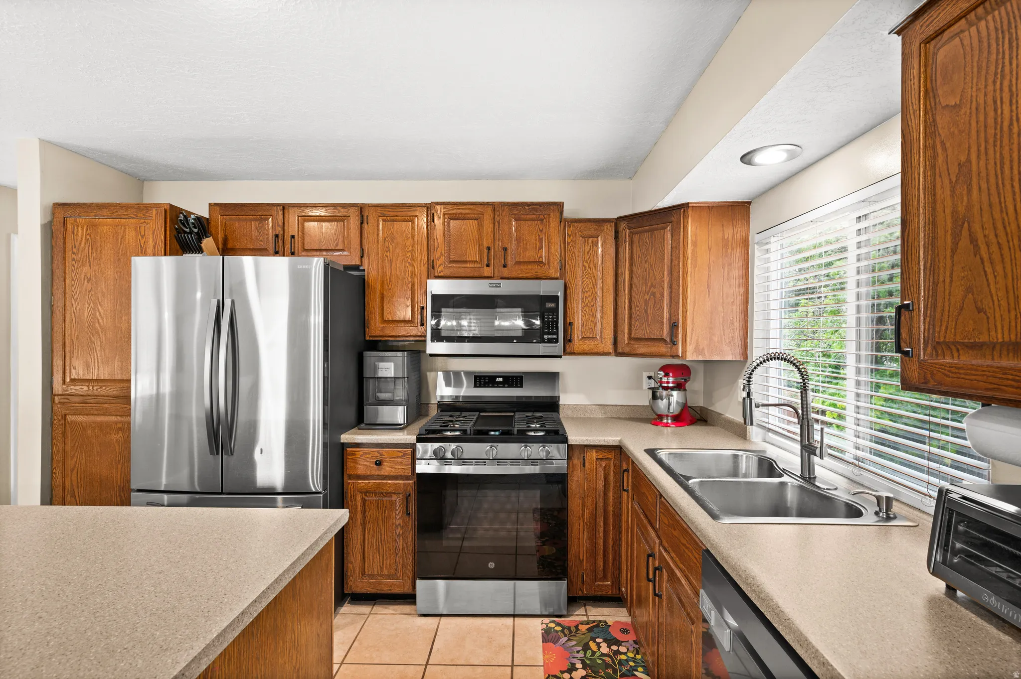 Kitchen featuring wood cabinetry, stainless steel appliances, a dual basin stainless steel sink, and light-toned countertops
