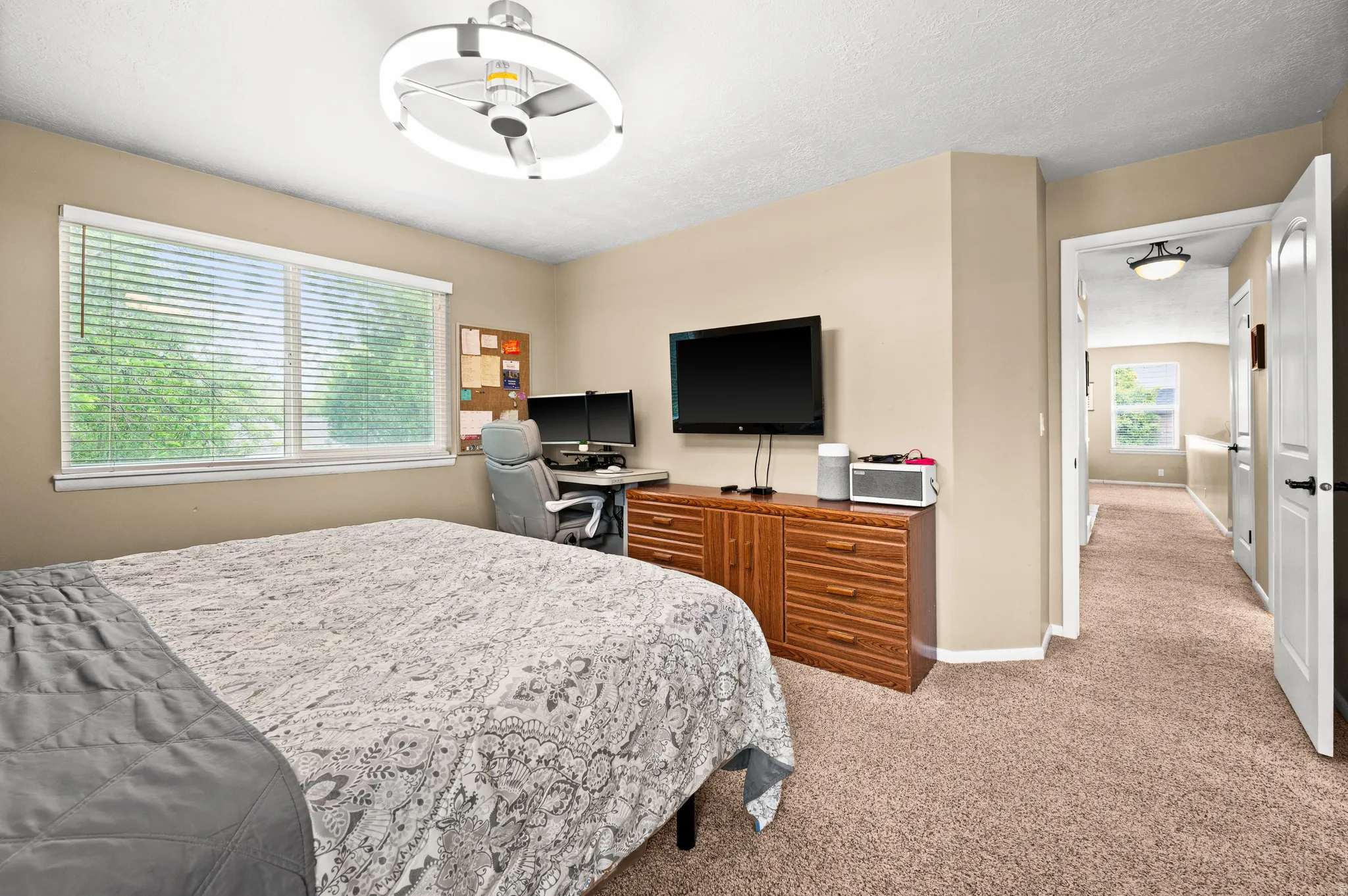 Carpeted interior room featuring a large window with blinds, a modern ceiling fan with integrated lighting, and a built-in wood-finish cabinet