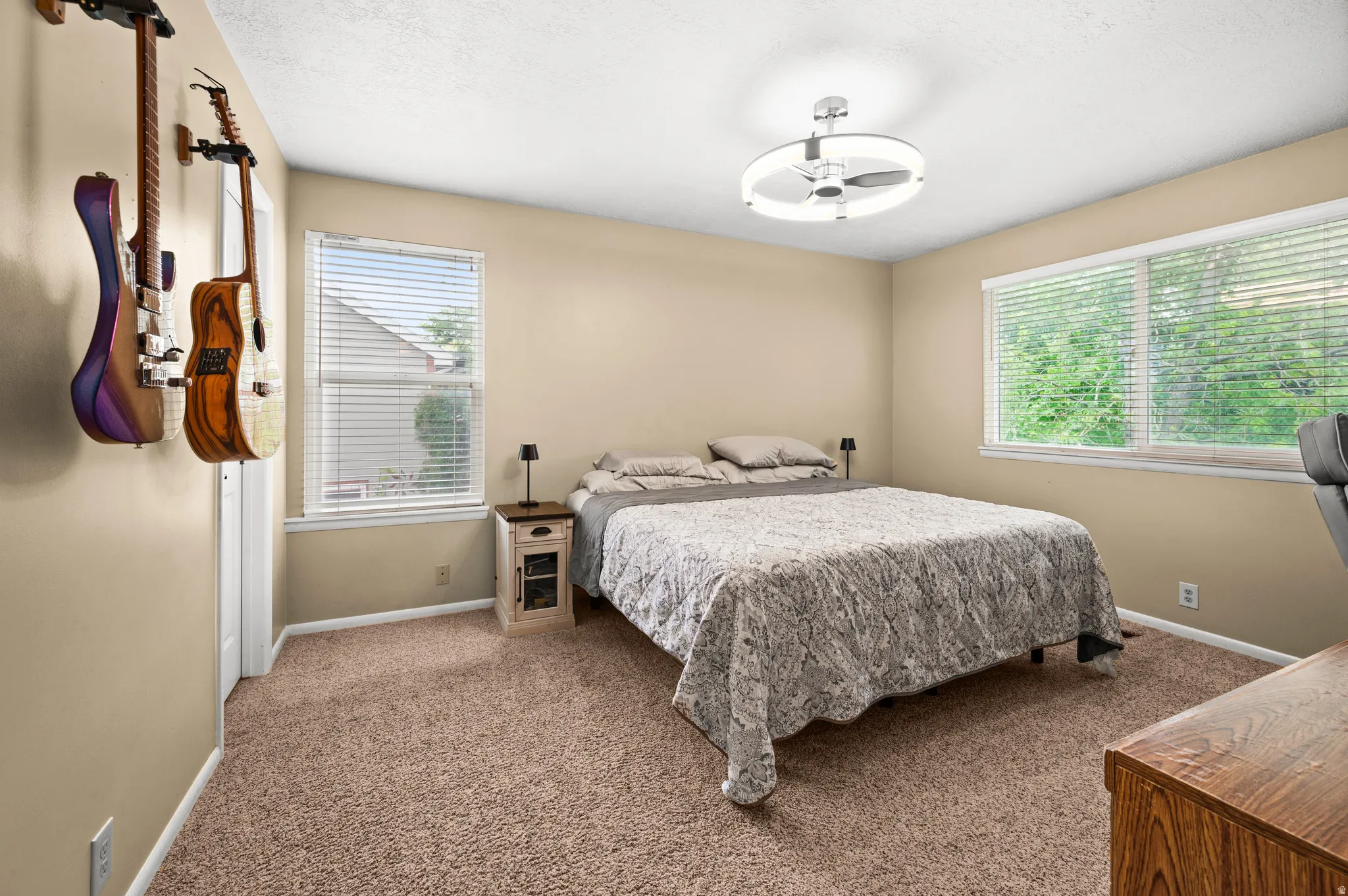 Carpeted interior room featuring two windows with blinds, a modern ceiling light fixture, and neutral wall paint
