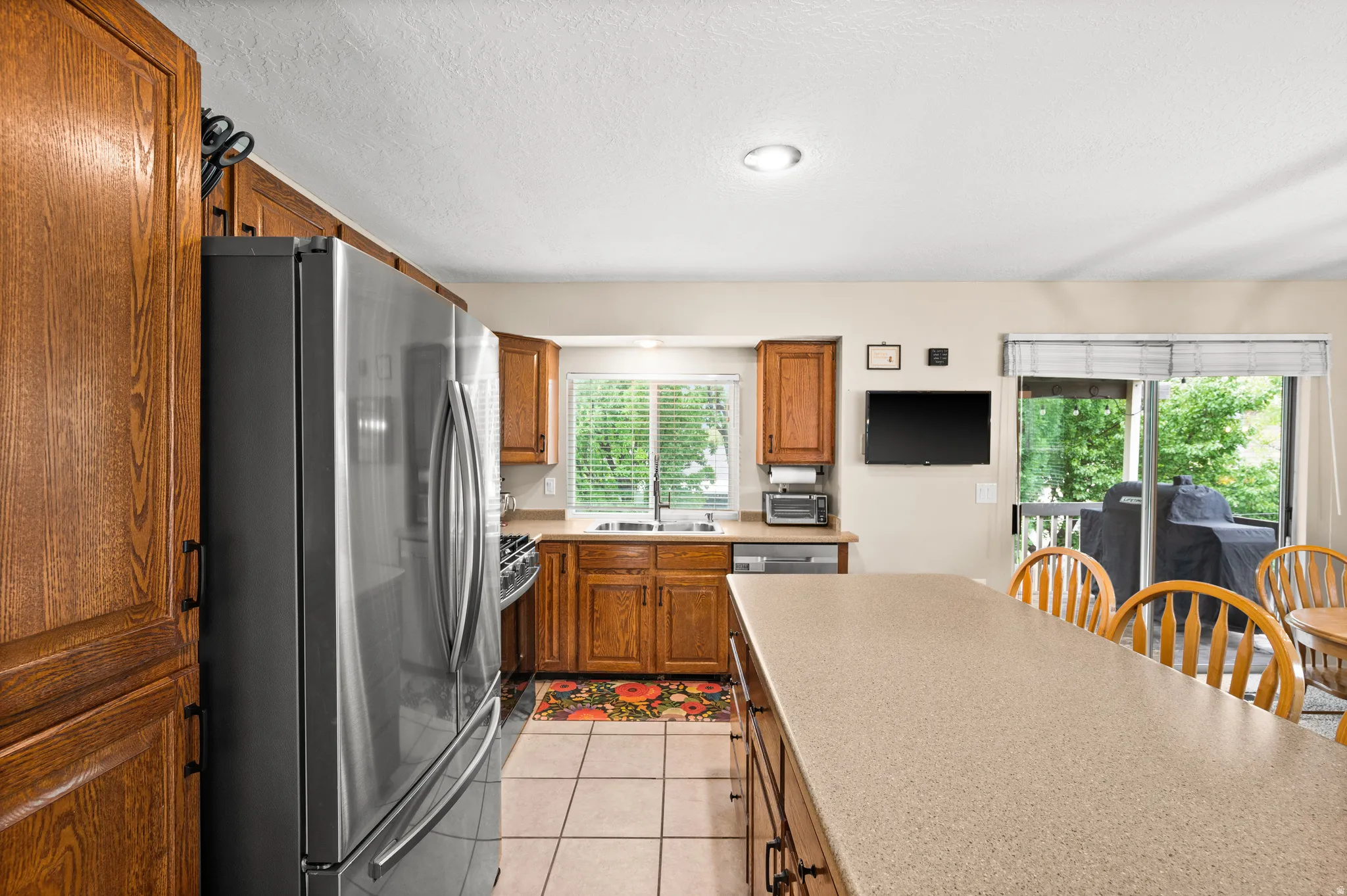 Kitchen featuring wood cabinetry, stainless steel appliances, a light-toned countertop island, tile flooring, and a sliding glass door leading to the exterior