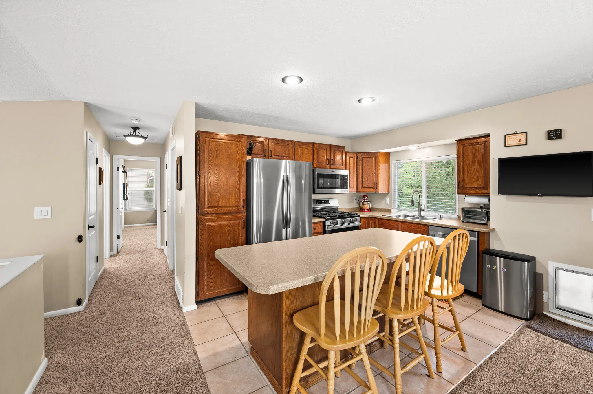Kitchen featuring wood cabinetry, stainless steel appliances, a counter-height island with seating, a window above the sink, and recessed lighting