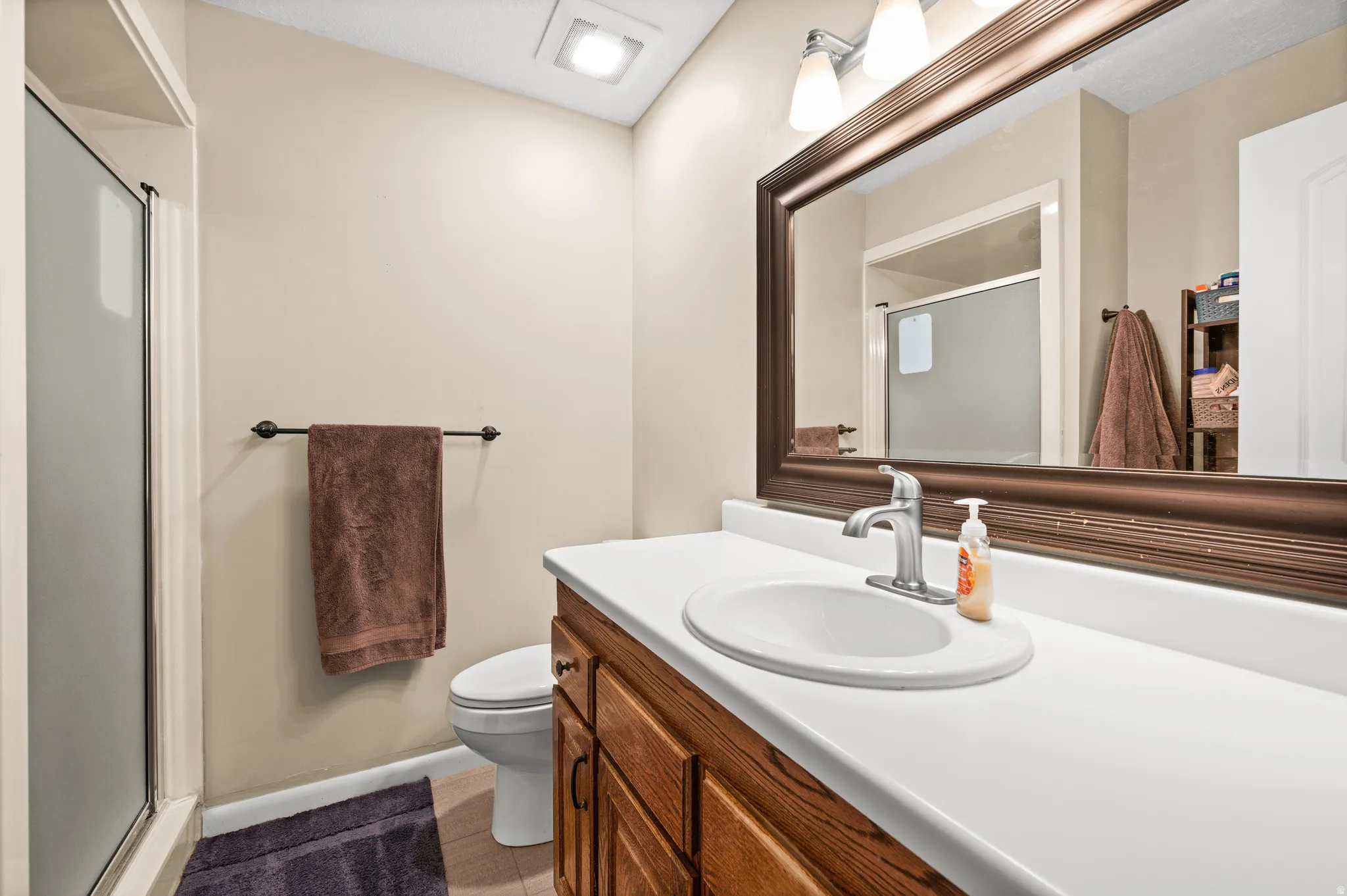 Bathroom featuring a wood-finish vanity with a white countertop and an oval undermount sink, illuminated by a three-light fixture above a framed mirror