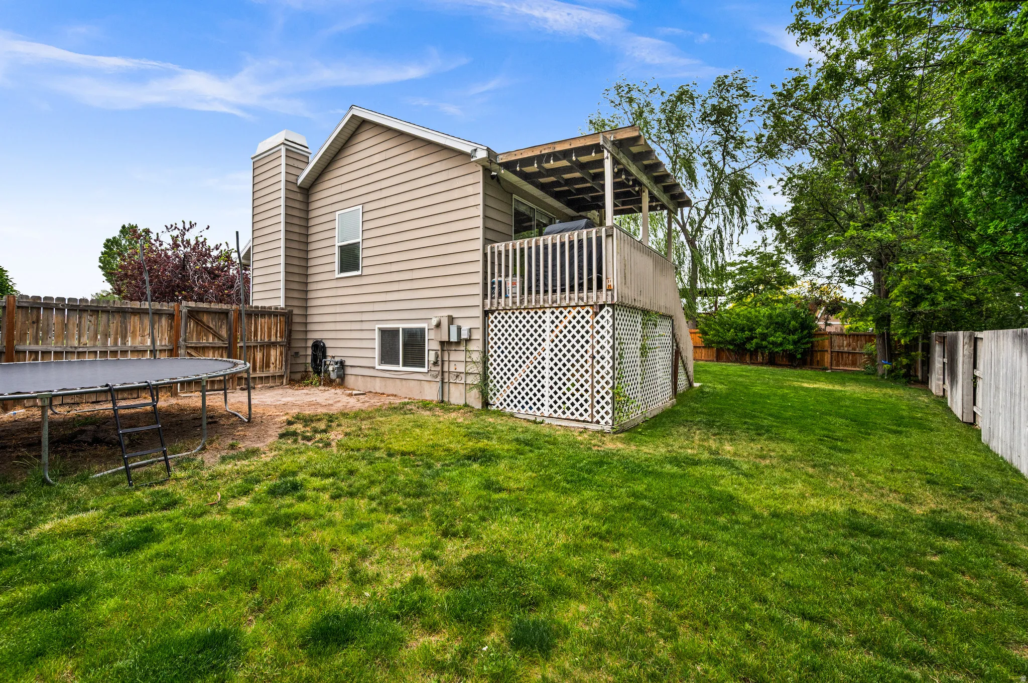 Expansive grassy backyard featuring a wooden privacy fence, a raised deck with wood railing and lattice skirting, and a tan siding exterior