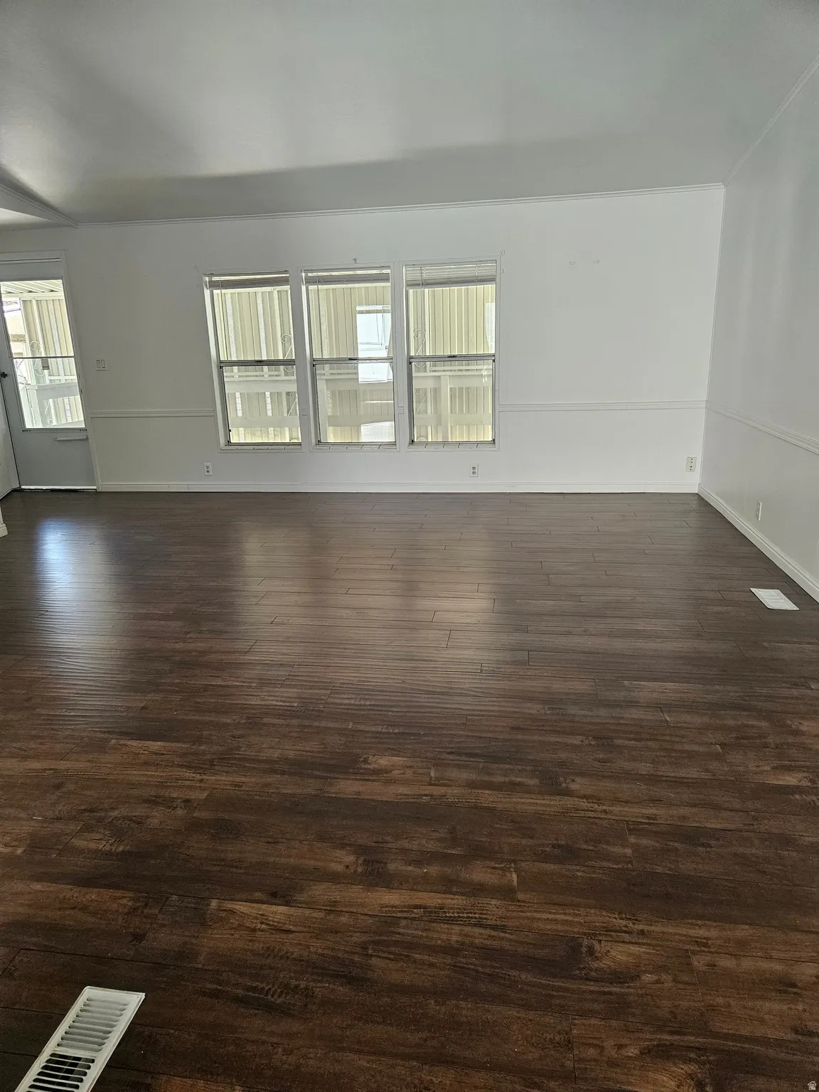 Spacious interior featuring wood-finish flooring, white walls, and a triple window assembly