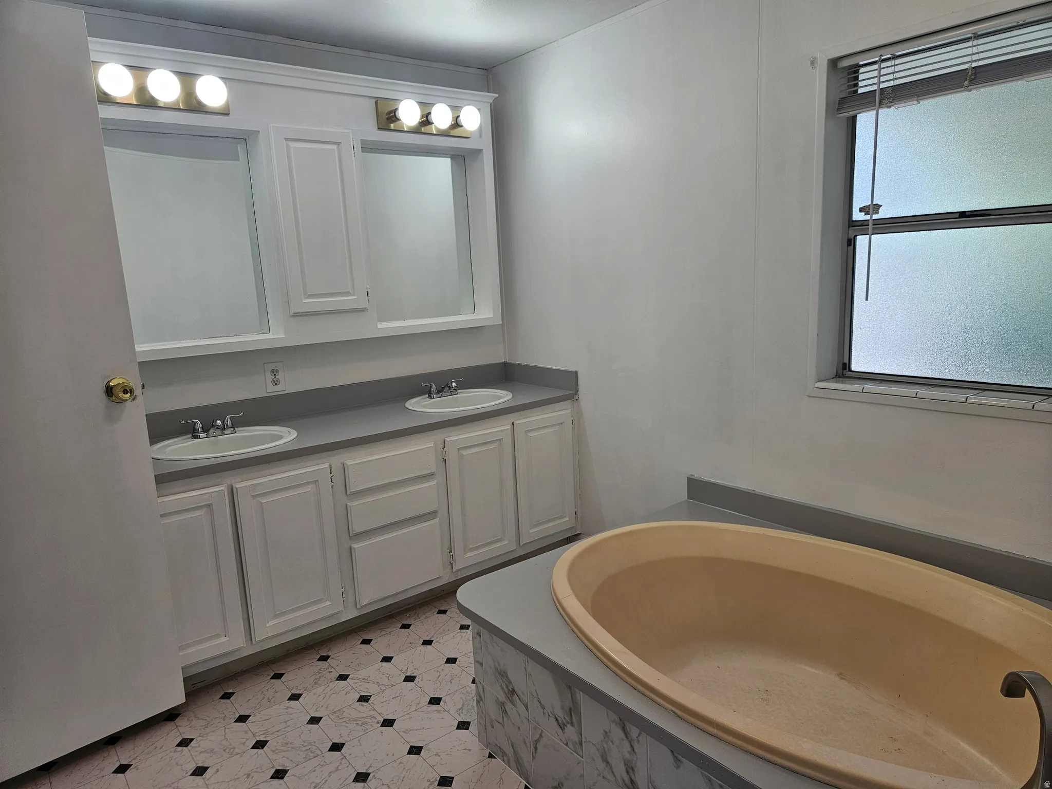 Bathroom featuring a built-in soaking tub, dual vanity with white cabinetry, and patterned flooring