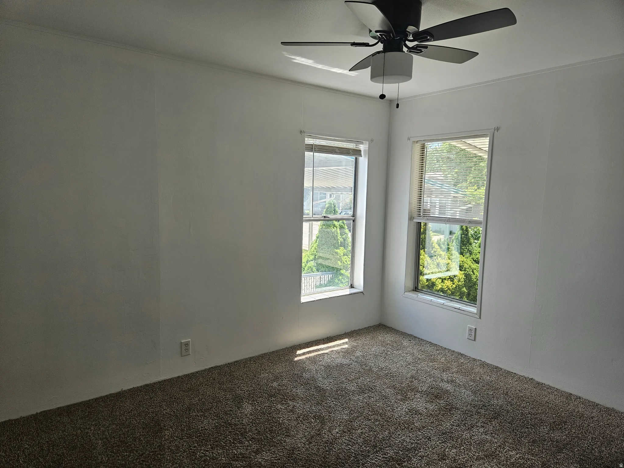 Room with neutral wall paint, two windows with blinds, and a dark-toned ceiling fan