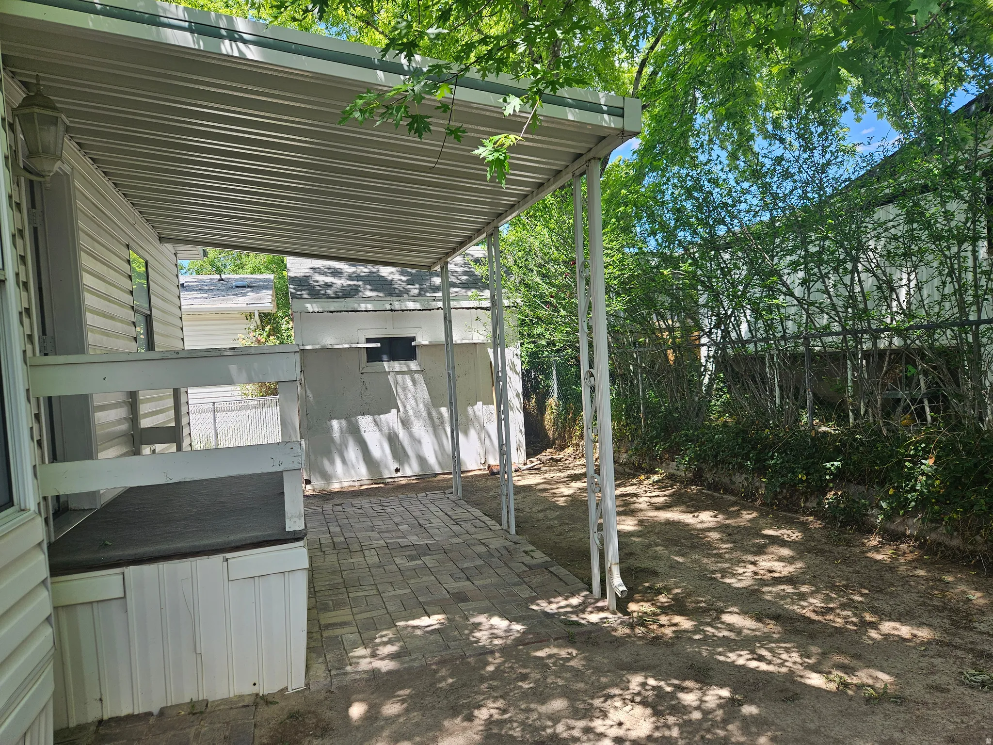 Covered patio with paver flooring, supported by white metal posts, offering an outdoor living area