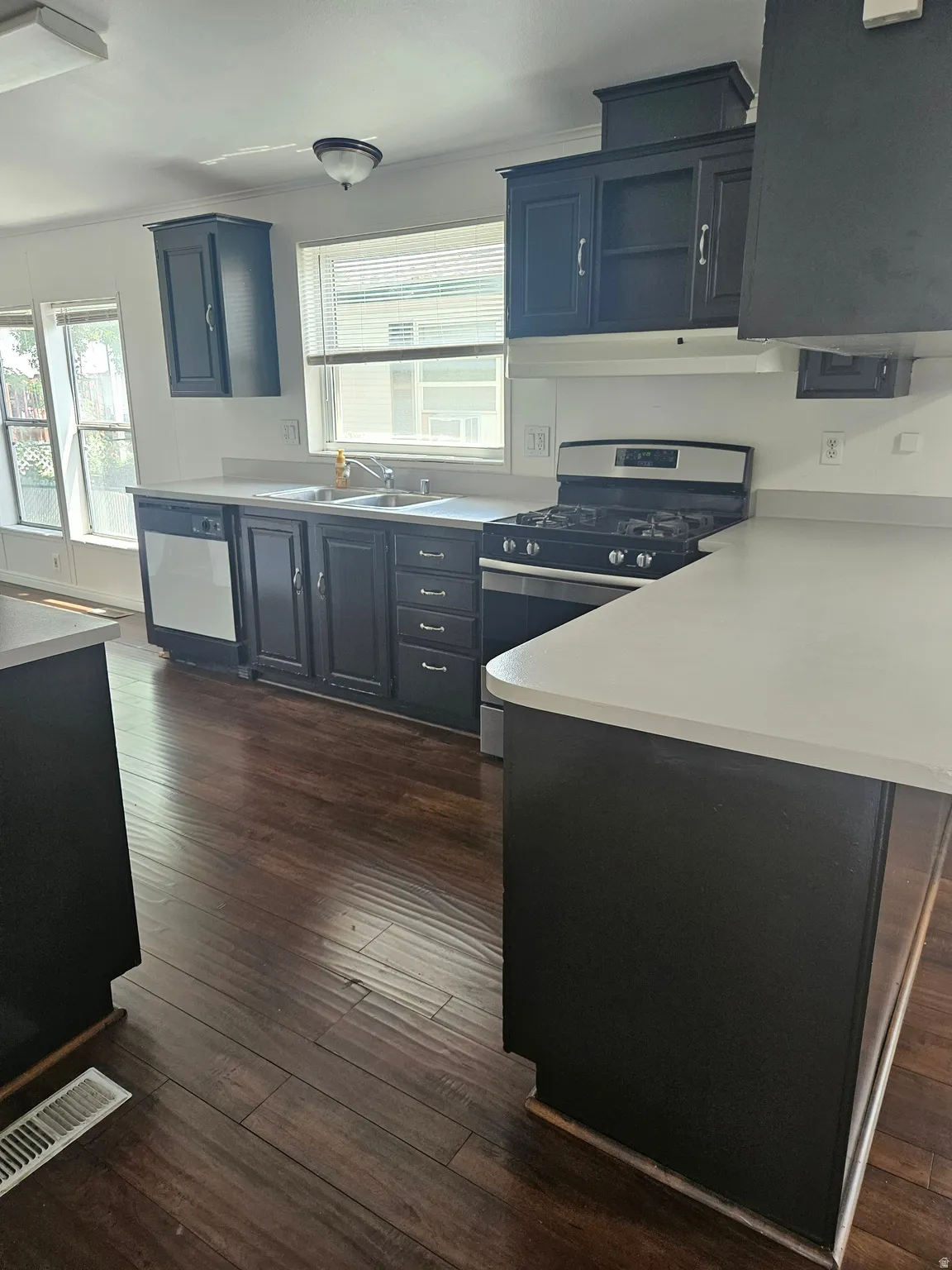 Kitchen featuring dark wood-finish flooring, dark cabinetry with silver hardware, light countertops, and a stainless steel range