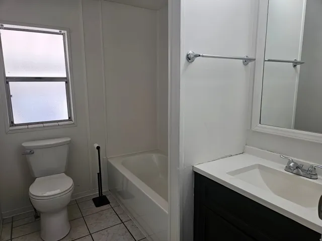 Bathroom featuring a white toilet, white bathtub, and a dark wood-finish vanity with an integrated white sink