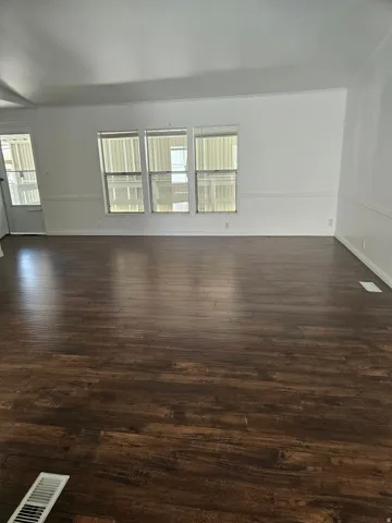 Spacious interior featuring wood-finish flooring, white walls, and a triple window assembly