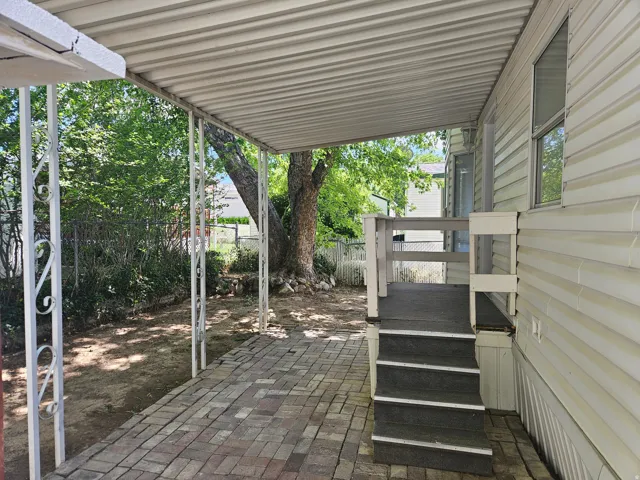 Covered patio featuring brick paver flooring, white metal support posts with decorative scrollwork, and a three-step entry to the structure