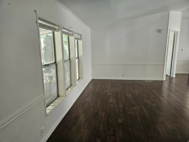 Open interior space featuring dark wood-finish flooring, white paneling, and a trio of windows providing natural illumination