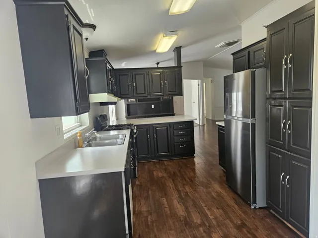 Kitchen featuring dark cabinetry, stainless steel appliances, a double basin sink, light countertops, and wood-finish flooring