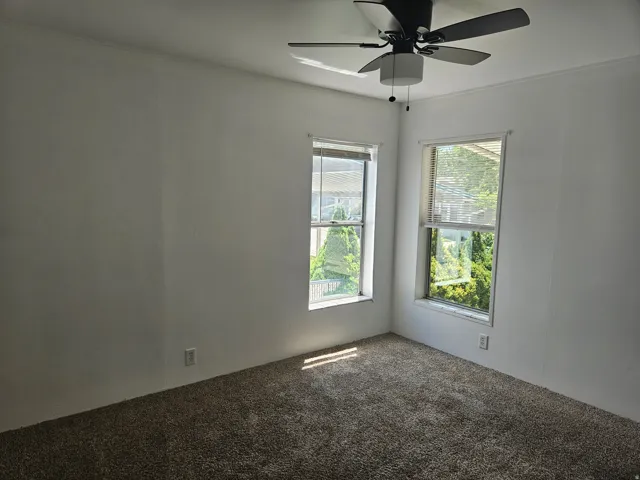 Room with neutral wall paint, two windows with blinds, and a dark-toned ceiling fan