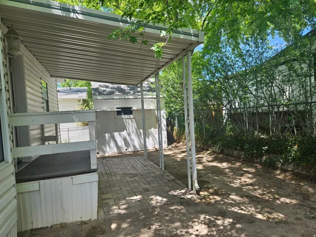 Covered patio with paver flooring, supported by white metal posts, offering an outdoor living area