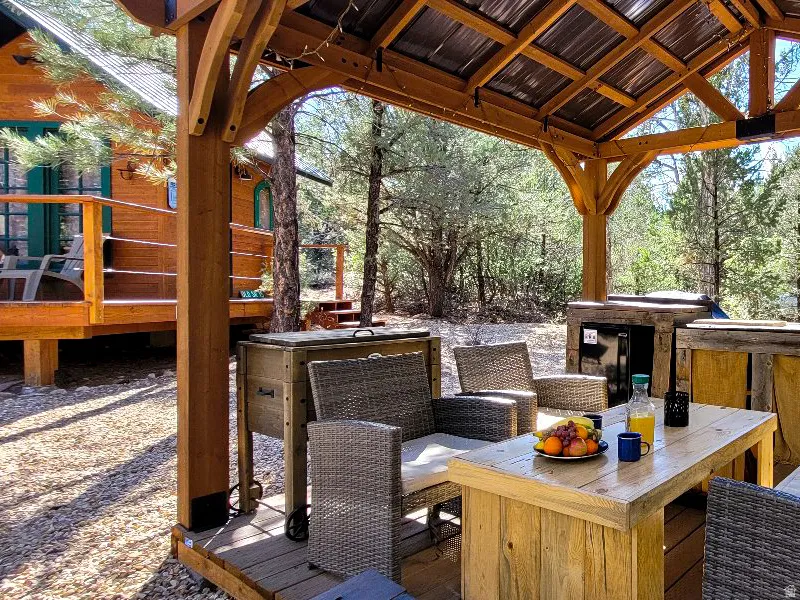 Wood-frame gazebo with a corrugated metal roof and exposed beams, featuring a wood-plank deck, built-in outdoor cabinetry, and a surrounding natural landscape
