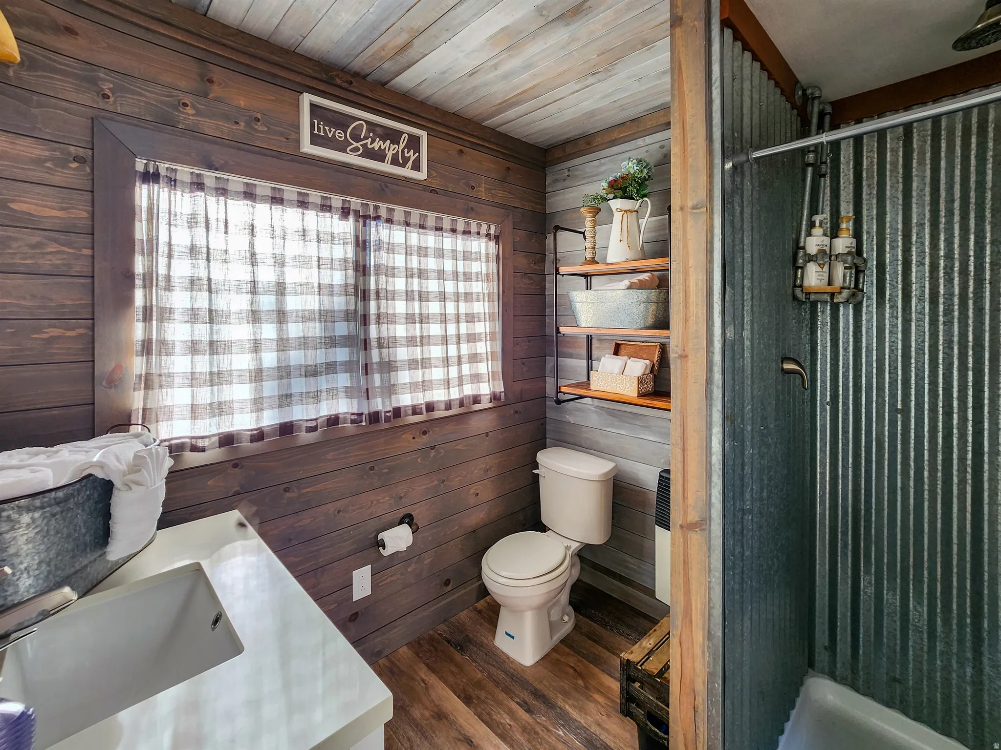 Bathroom featuring wood-finish wall paneling, wood-finish flooring, a white vanity with an undermount sink, and a shower with corrugated metal walls