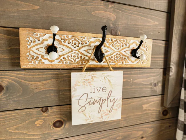 Wood-paneled wall featuring a decorative carved wood coat rack with three hooks